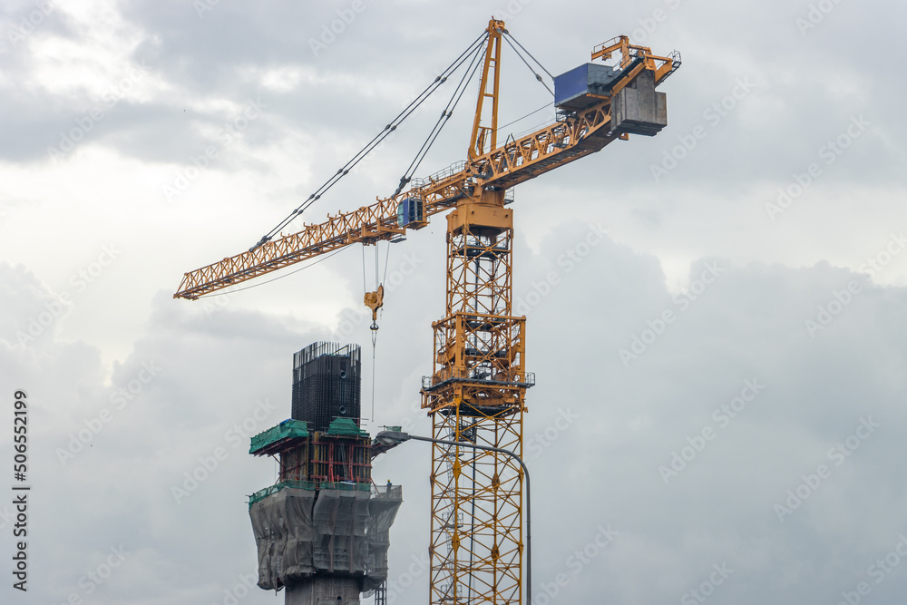 Construction of a concrete pillar using a high-rise crane, on a background of rainy clouds Construction of a concrete pillar using a high-rise crane, on a background of rainy clouds
