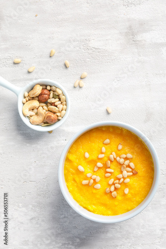 Overhead view of cream soup served with nuts on light grey concrete background