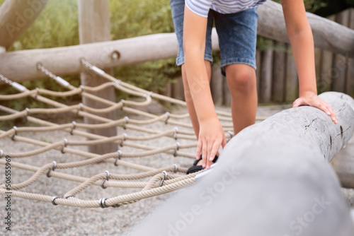 Cute blond boy climbing on a wooden playground in a rope park.