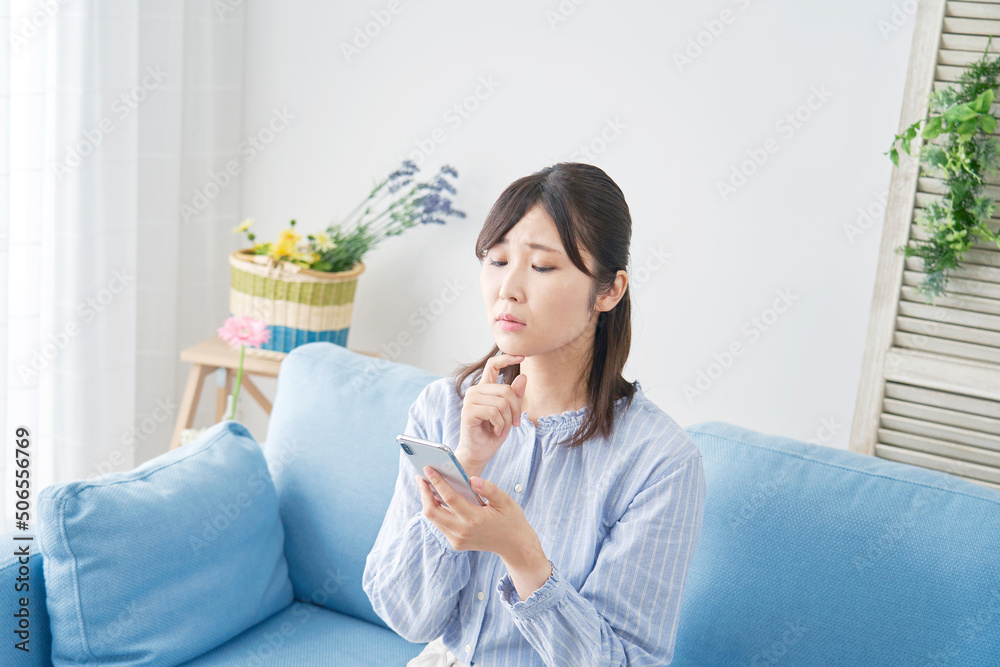 リビングでスマホを見ながら悩む女性