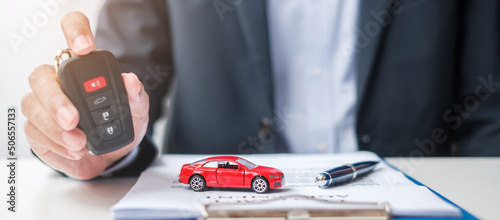 Businessman hand holding remote keyless with car toy, pen and contract document. buy and sale, insurance, rental and contract agreement concepts photo