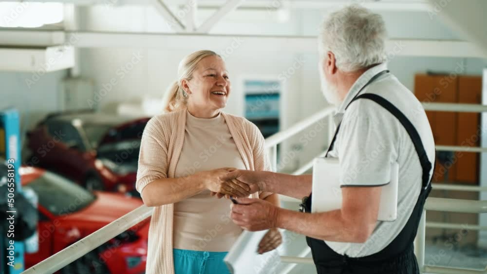 Adult female insurance agent shakes hands with the mechanic at the car service.