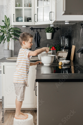 The boy prepares dough for biscuit or baking in the kitchen. The child mixes the ingredients with a whisk. Little chef and helper. vertical photo