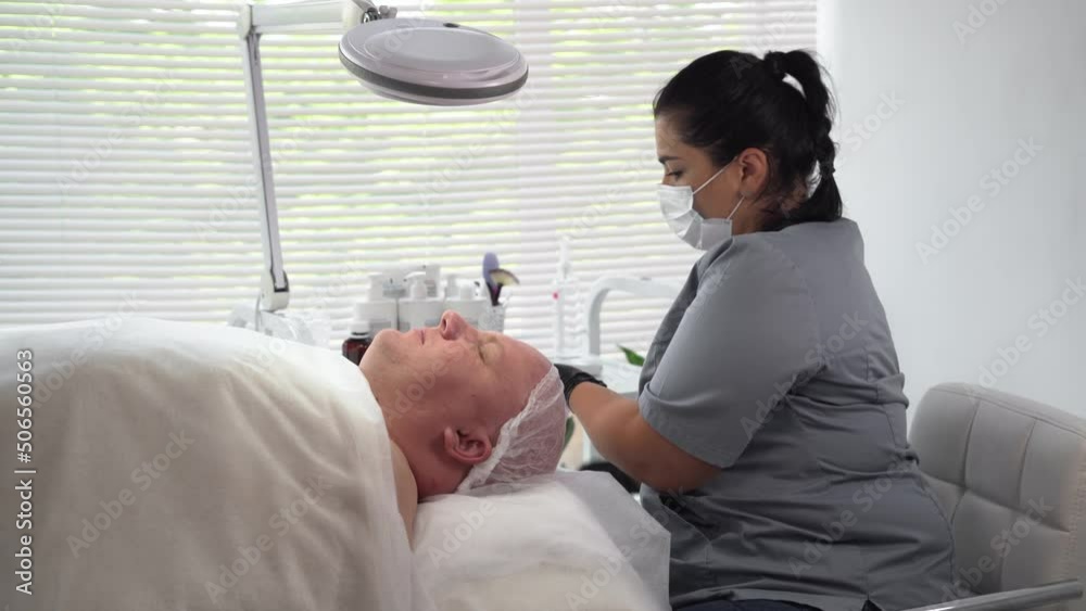 Cosmetologist applying cosmetic mask on man's face in spa salon Cosmetologist applying cosmetic mask on man's face in spa salon