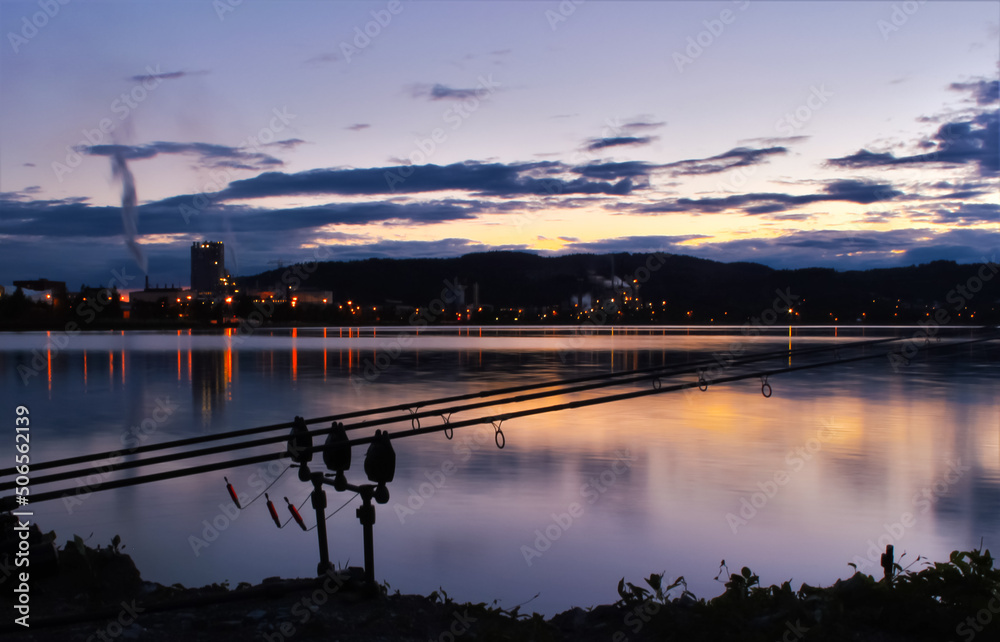 Carp fishing rods and gear by an urban lake during sunset. Sunset and carp angling. Shallow depth of field.