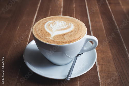 Large white cup of cappuccino with a pattern on milk foam on a wooden table, toned photo
