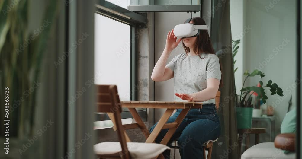 Young woman sitting on the balcony experiencing virtual reality in the metaverse Young woman sitting on the balcony experiencing virtual reality in the metaverse