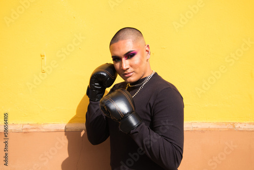 Fotografie Young non-binary person wears boxing gloves on a mustard yellow background, the person is make up and does different boxing poses