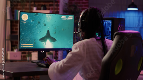 Fotografie, Obraz Over shoulder view of african american gamer girl playing space shooter simulation using pc gaming setup enjoying free time at home