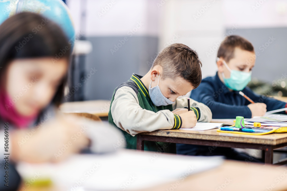 Profile of a pupil writing down schoolwork in notebook while sitting in classroom during covid 19. Profile of a pupil writing down schoolwork in notebook while sitting in classroom during covid 19.