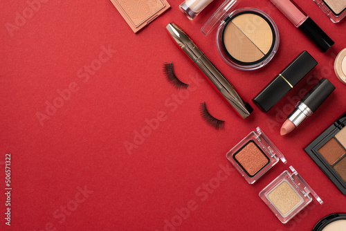 Makeup concept. Top view photo of lipstick lip gloss contouring palette eyeshadow blush mascara and false eyelashes on isolated red background with copyspace