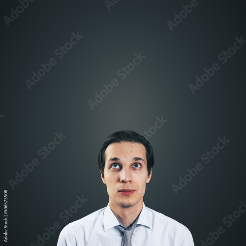 Man looking up in white shirt and tie isolated on blank dark grey background with empty space for your text or logo  mockup. Thinking and brainstorming concept  close up