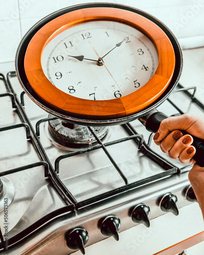 A female hand holds the handle of a frying pan with a wall clock inside, as she puts it on the stove photo