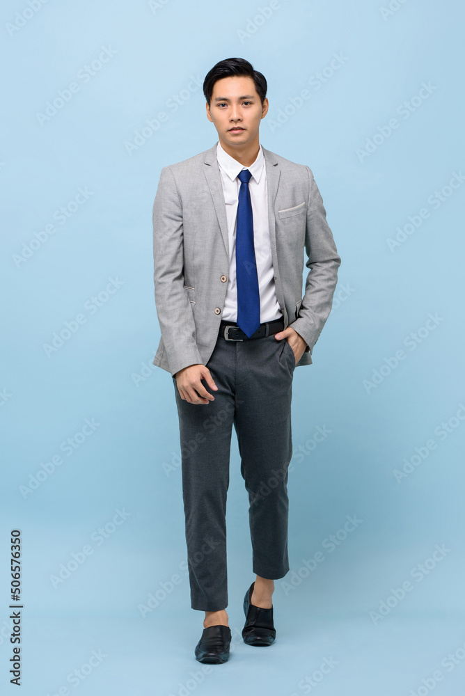 Asian man wearing business suit with modern ankle pants walking in light blue studio isolated background Asian man wearing business suit with modern ankle pants walking in light blue studio isolated background