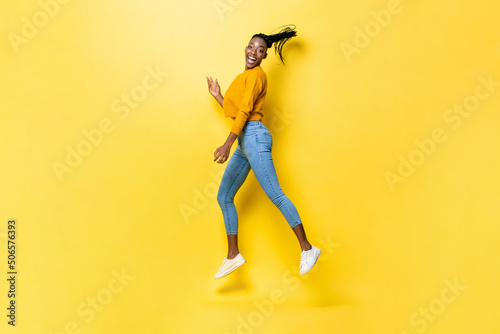 Energetic happy African American woman jumping and smiling in yellow isolated studio background