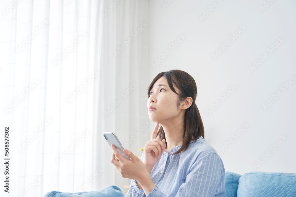 リビングでスマホを持って考える女性 リビングでスマホを持って考える女性