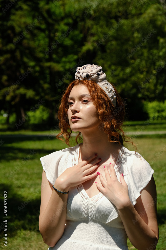 Naklejka premium Elegant young red hair lady in a white summer dress in a park