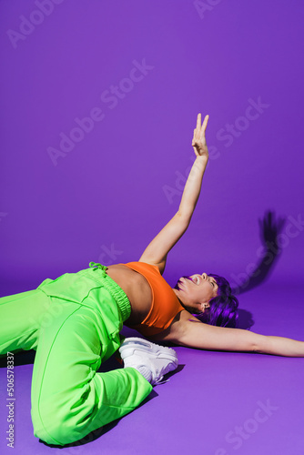 Carefree woman dancer wearing colorful sportswear performing against purple background