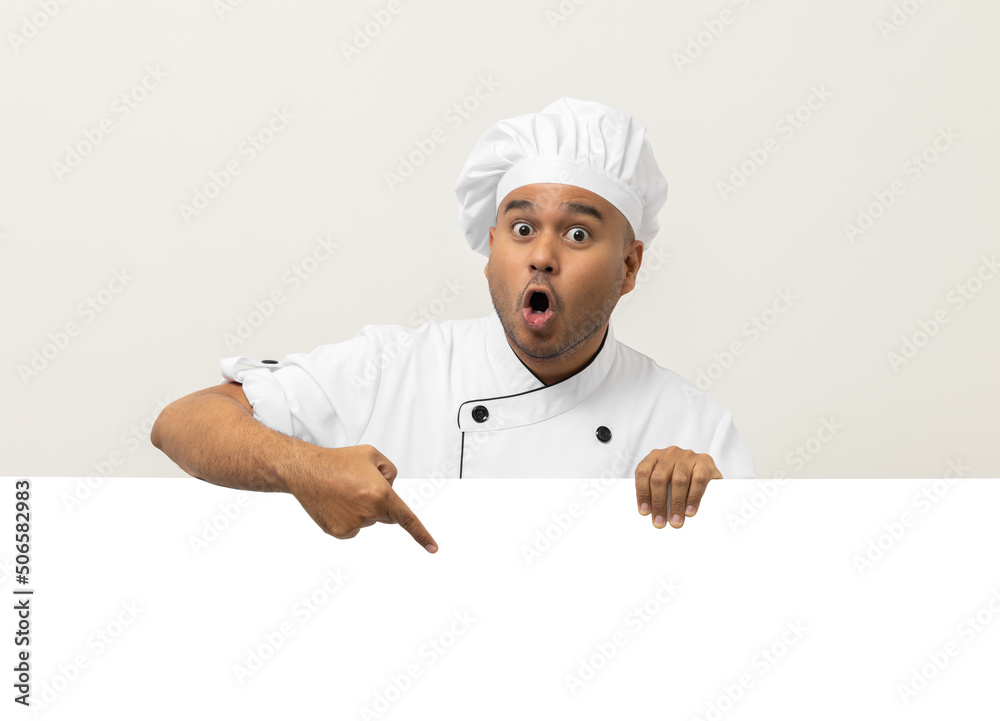 Happy Young handsome asian man chef in uniform looks out from behind an empty whiteboard. Cooking indian man hiding behind big blank billboard for advertising text menu in kitchen and restaurant. Happy Young handsome asian man chef in uniform looks out from behind an empty whiteboard. Cooking indian man hiding behind big blank billboard for advertising text menu in kitchen and restaurant.