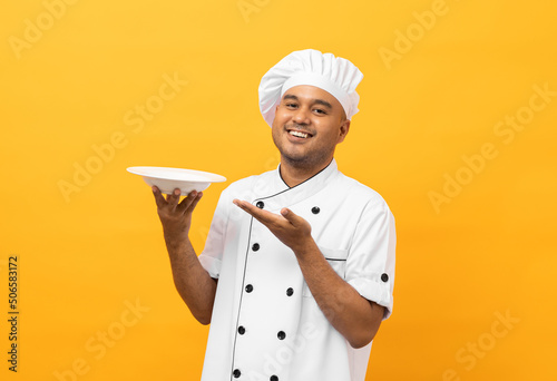 Fotografie Attractive Young handsome asian man chef in uniform holding empty plate delicious dish menu good taste on isolated