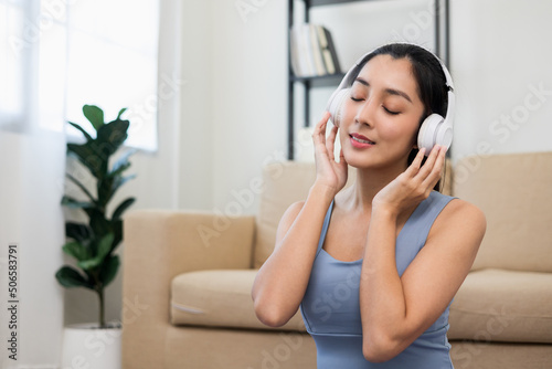 Beautiful asian woman in sportswear put on headphone listening music relax after workout. Cheerfully sporty female workout and exercise wearing sport wear at home.