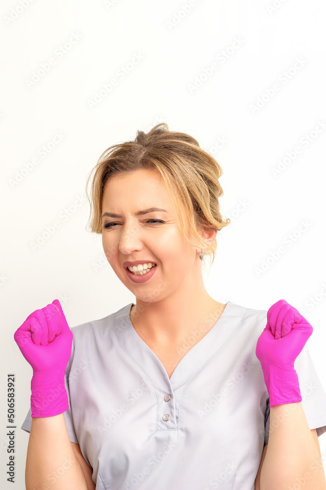 Happy caucasian woman doctor wearing pink gloves celebrates and raising fists on white background Happy caucasian woman doctor wearing pink gloves celebrates and raising fists on white background