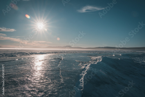 Cracks in the ice of Lake Storsjö looking onto Storådörren during melting winter times. Crevasse leading towards spruce trees and horizon. Copy space included.