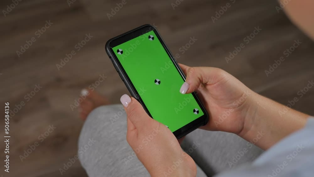 Close-up of a woman holding a phone with a green screen while sitting at home on the couch. Chroma key.