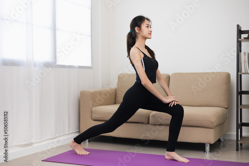 Young asian sport woman sitting practicing yoga lesson. Stretching leg training workout on yoga mat at home for good health and body shape.