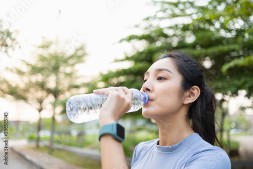 Happy slim woman drinking water after workout exercising in the city at sunrise. Young beautiful asian drinking water after jogging running outdoor. Healthy and active lifestyle concept.