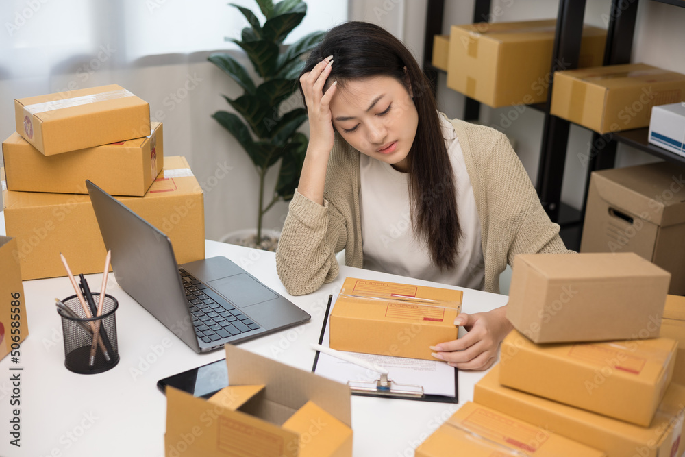 Busy and stressed asian entrepreneur woman checking product on stock working with laptop. Business woman working SME online at home. Small business owner start up freelance concept. Busy and stressed asian entrepreneur woman checking product on stock working with laptop. Business woman working SME online at home. Small business owner start up freelance concept.