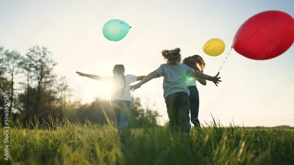 Happy family with balloons run through park. Silhouette of children at sunset in backyard. Group of children are playing on green grass in garden. Child birthday. People running with colored balloons Happy family with balloons run through park. Silhouette of children at sunset in backyard. Group of children are playing on green grass in garden. Child birthday. People running with colored balloons