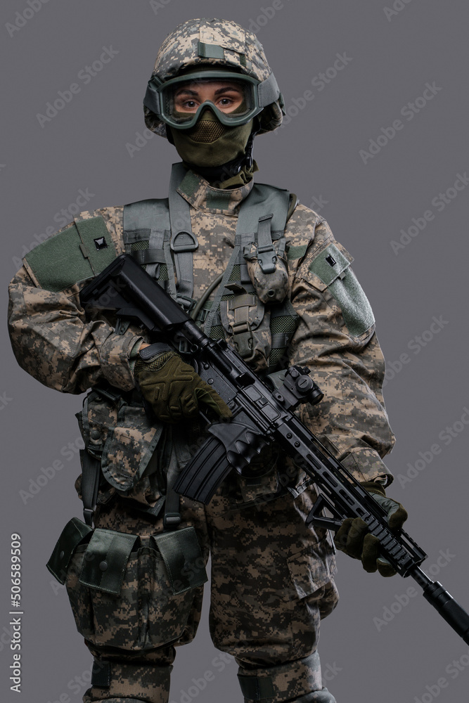 Portrait of professional servicewoman with rifle dressed in camouflage clothes against grey background. Portrait of professional servicewoman with rifle dressed in camouflage clothes against grey background.