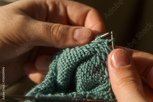 Close-up hand knitting. Hobbies, handicrafts. Knitting warm clothes from woolen fine yarn by hand on metal needles. Selective focus