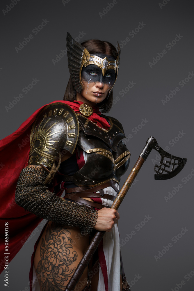 Fototapeta premium Shot of female viking warrior with axe and tattooed body isolated on grey background.