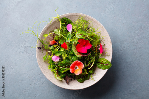 Green salad leaves, sprouts with edible flowers in bowl. Grey background. Close up. Top view. photo