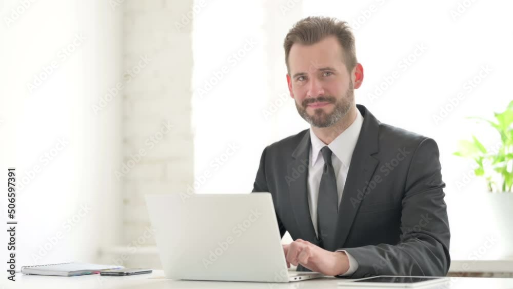 Young Businessman Showing Thumbs Up Sign While using Laptop in Office Young Businessman Showing Thumbs Up Sign While using Laptop in Office