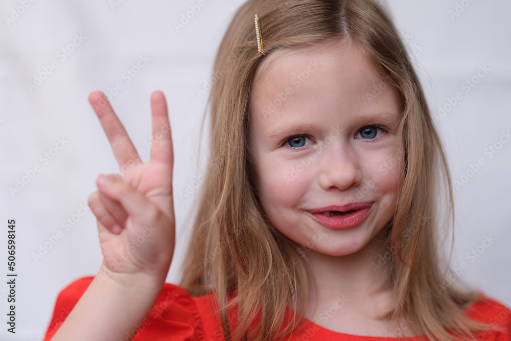 Portrait of little blonde girl with two fingers gesture.