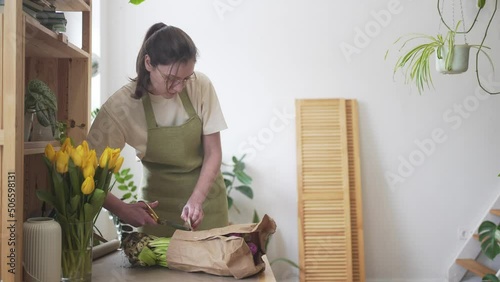A professional florist cuts a bouquet of fresh flowers in craft paper with scissors. Flower shop employee at work, businesswoman