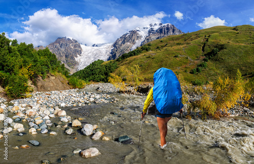 A man with a large backpack is fording a fast mountain river. Georgia.Svaneti photo
