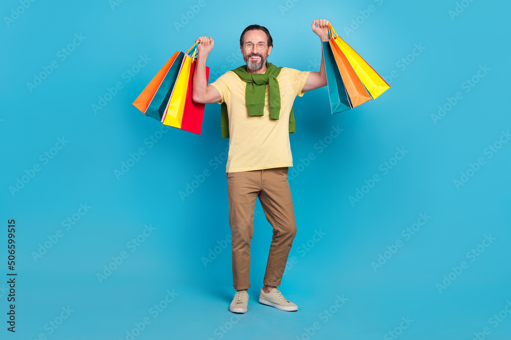 Full length portrait of cheerful person hold raise packages enjoy free time isolated on blue color background