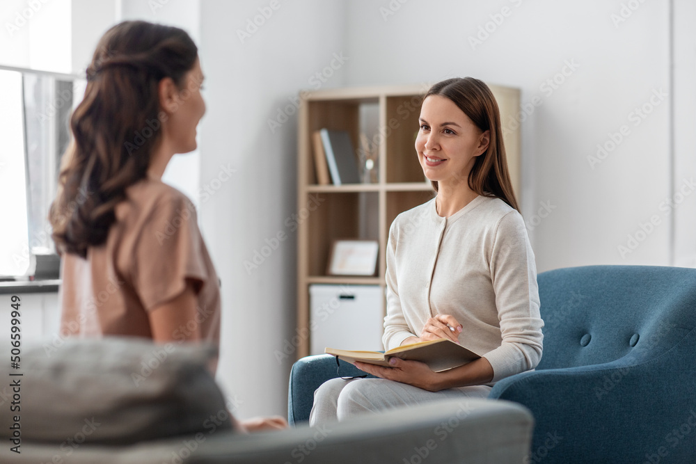psychology, mental health and people concept - smiling psychologist with notebook and woman patient at psychotherapy session - obrazy, fototapety, plakaty 