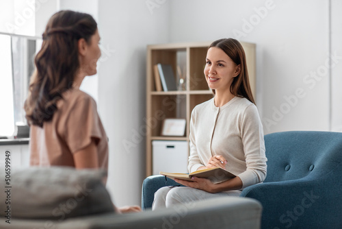 psychology, mental health and people concept - smiling psychologist with notebook and woman patient at psychotherapy session photo