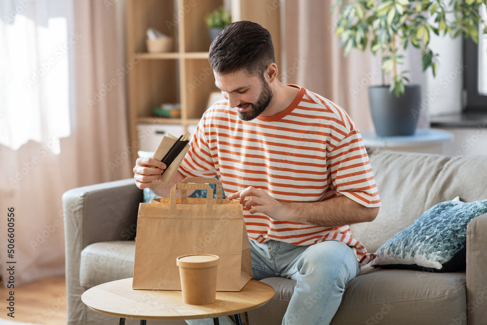 consumption, eating and people concept - smiling man unpacking takeaway food in paper bag at home consumption, eating and people concept - smiling man unpacking takeaway food in paper bag at home