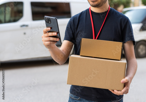 Detalle de repartidor, mirando el teléfono móvil, con las cajas de cartón, para ver ubicación de la entrega. photo