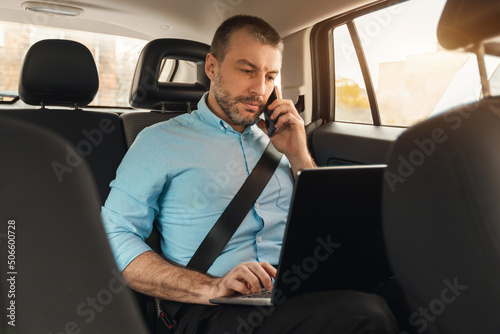 Businessman using laptop talking on smartphone while going by car © Prostock-studio