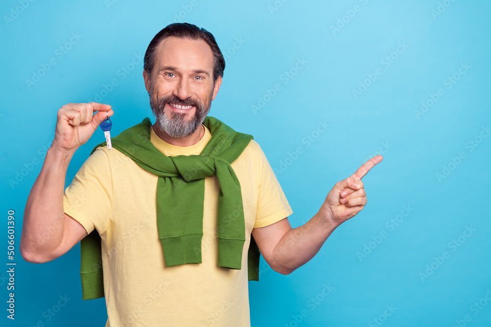 Photo of positive person demonstrate hold key indicate finger empty space isolated on blue color background Photo of positive person demonstrate hold key indicate finger empty space isolated on blue color background