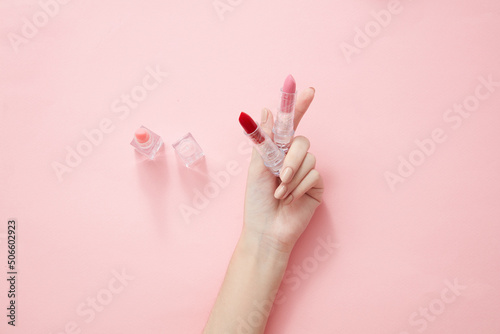 Top view of hand model holding lipstick in pink background for cosmetic advertising