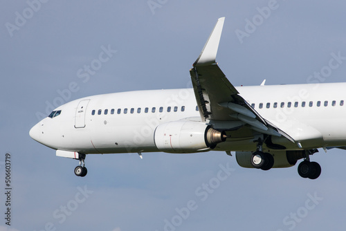 Full white neutralized airliner Boeing 737-800 landing at an airport in front of clear blue sky