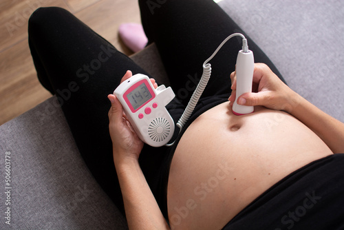 Tableau sur toile Pregnant woman with a fetal doppler listening to the baby's heart sitting on the